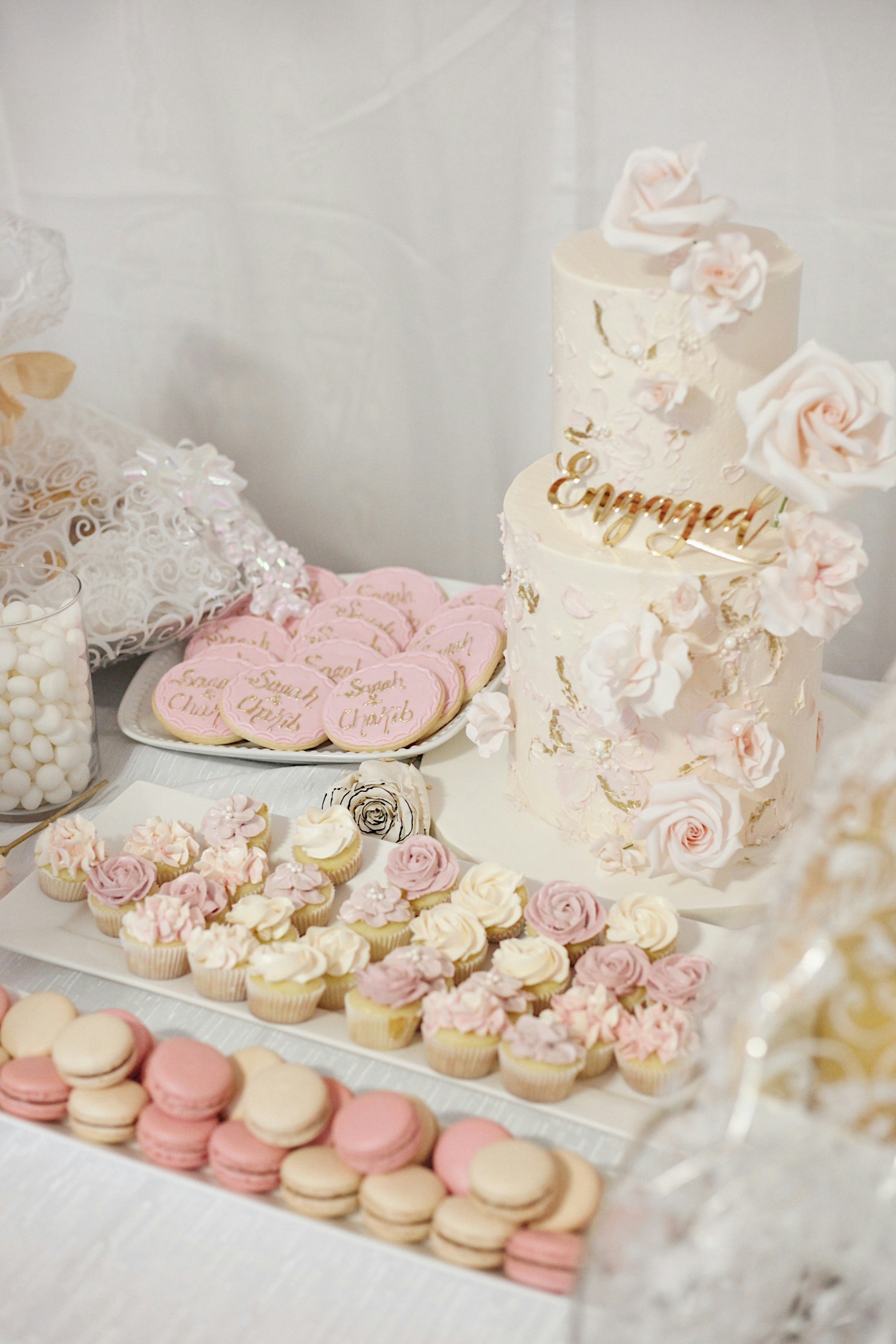 A pale celebration cake with roses, cupcakes, and macarons
