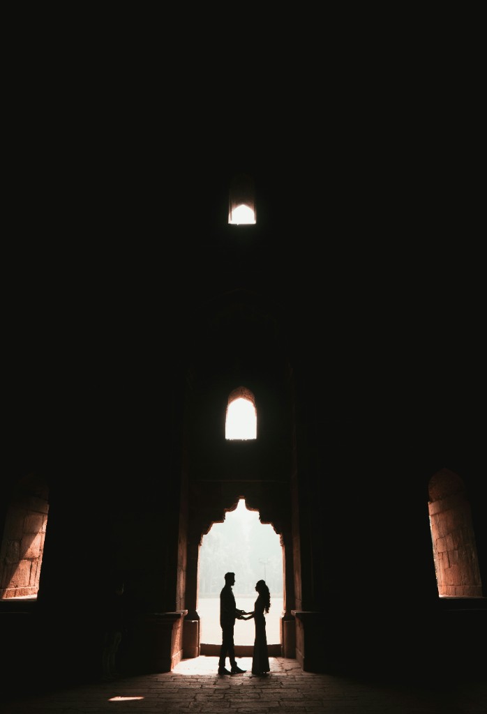 A couple in silhouette, holding hands inside a stone arch filled with light