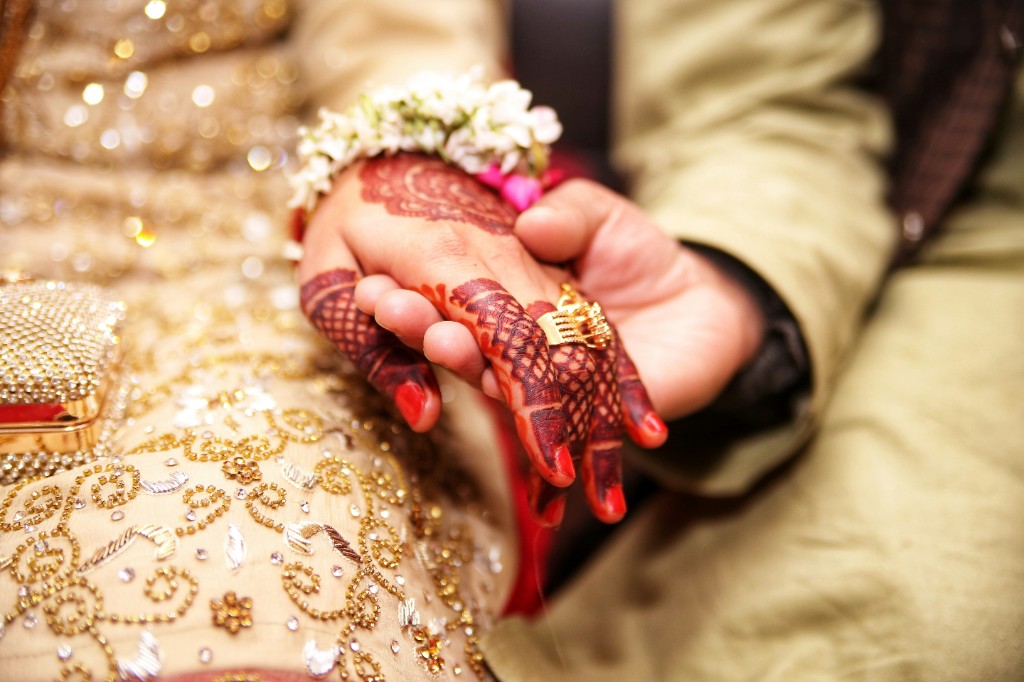 Mehndi-painted hands held together, with a gold ring and white flowers